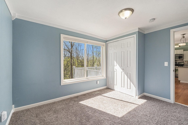 unfurnished bedroom featuring crown molding, carpet floors, baseboards, and a closet