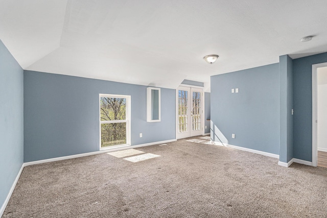 carpeted empty room with baseboards, vaulted ceiling, a smoke detector, and french doors