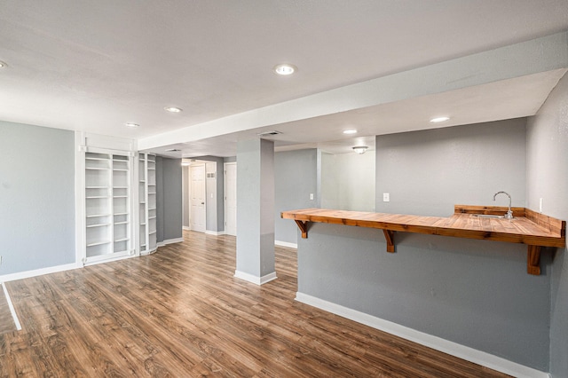 finished basement with baseboards, a sink, wood finished floors, built in shelves, and recessed lighting