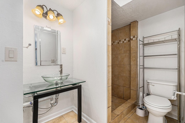 bathroom featuring a sink, tile patterned floors, a tile shower, toilet, and a textured ceiling