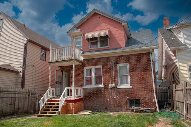 back of house featuring brick siding, a balcony, a fenced backyard, and roof with shingles