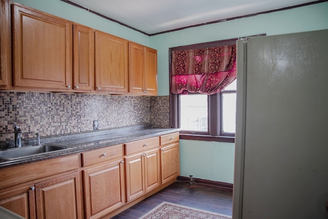 kitchen featuring a sink, dark wood-type flooring, tasteful backsplash, freestanding refrigerator, and crown molding