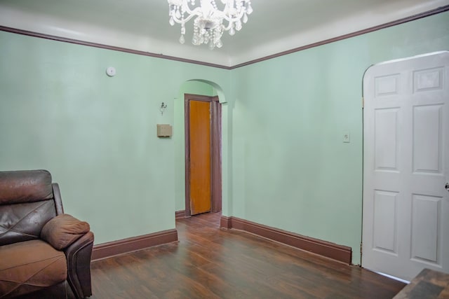living area featuring arched walkways, wood finished floors, baseboards, a chandelier, and crown molding