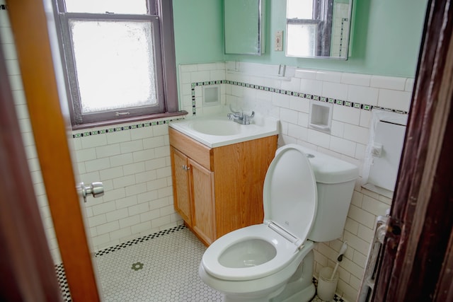 half bathroom featuring tile walls, toilet, wainscoting, tile patterned floors, and vanity