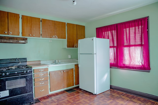 kitchen with freestanding refrigerator, black gas range oven, under cabinet range hood, a sink, and light countertops