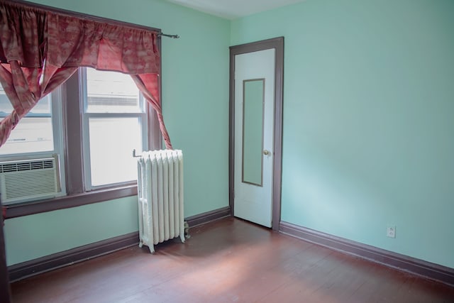 empty room featuring radiator heating unit, wood finished floors, baseboards, and cooling unit