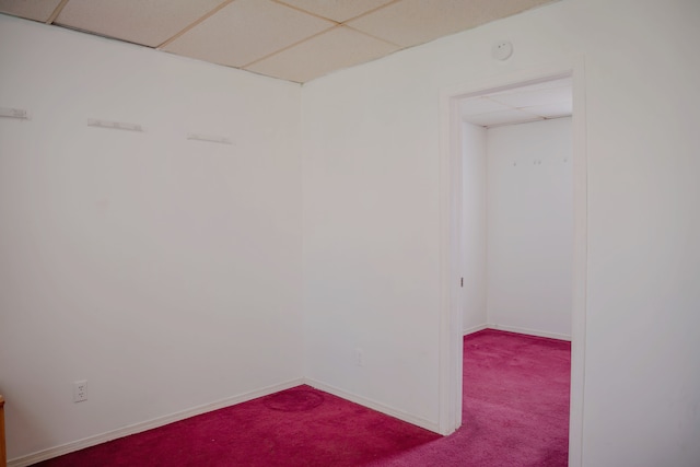 empty room featuring dark carpet, a paneled ceiling, and baseboards