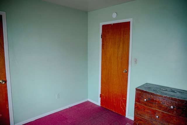 unfurnished bedroom with dark carpet and baseboards
