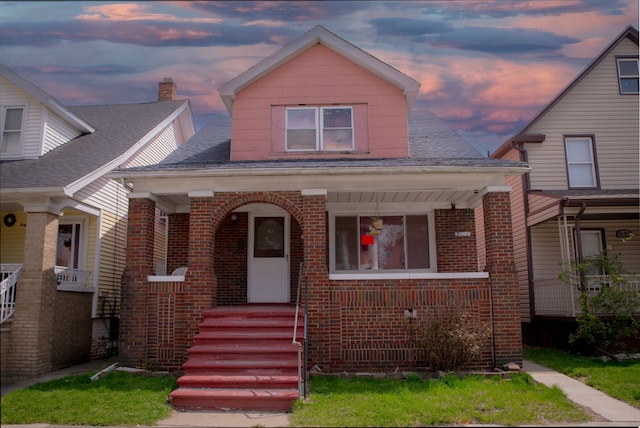 bungalow-style house featuring brick siding, covered porch, and a shingled roof