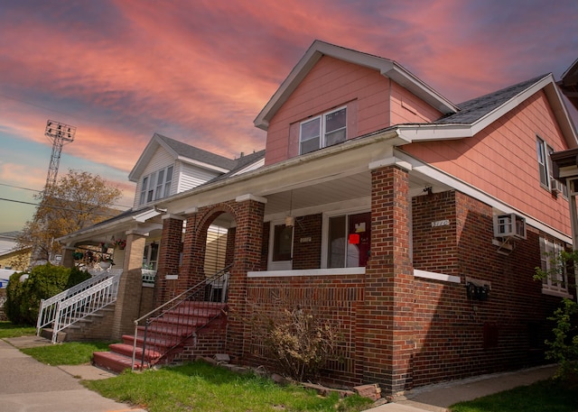 view of front of home featuring brick siding, a porch, and a wall mounted AC
