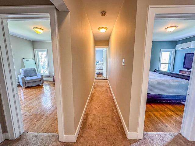 corridor featuring baseboards, an AC wall unit, wood finished floors, and carpet