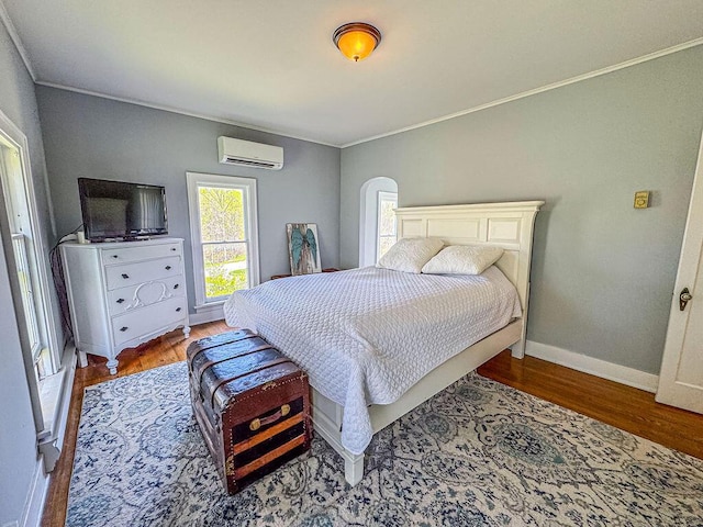 bedroom with crown molding, a wall mounted AC, wood finished floors, and baseboards