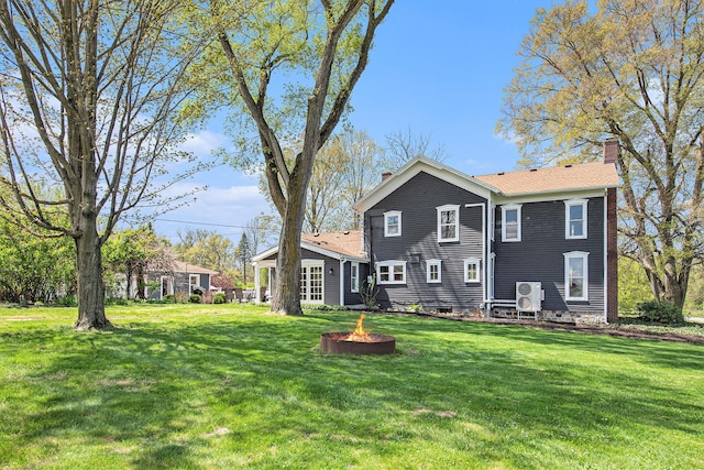 rear view of property featuring a chimney, an outdoor fire pit, and a yard
