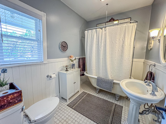 bathroom featuring toilet, a wainscoted wall, a bath, tile patterned floors, and a shower with curtain