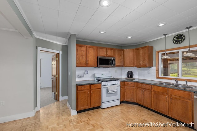 kitchen with stainless steel appliances, a sink, brown cabinets, dark countertops, and crown molding