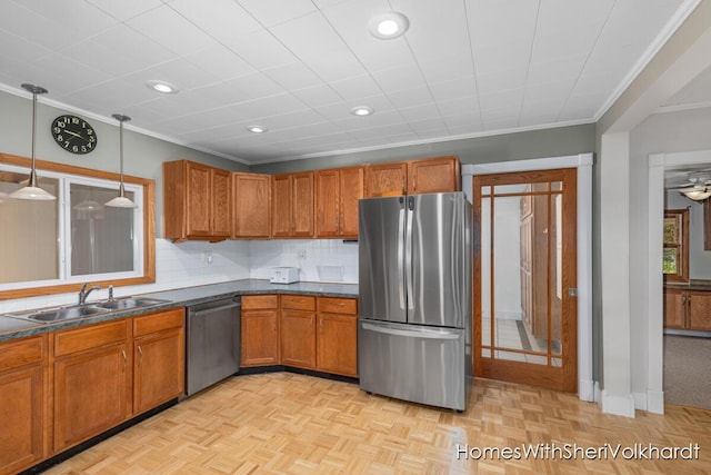 kitchen with stainless steel appliances, a sink, brown cabinetry, dark countertops, and crown molding