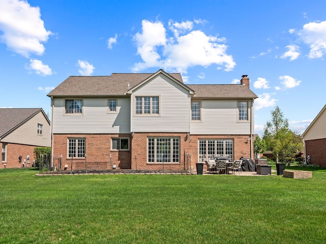 back of property with a chimney, brick siding, a patio area, and a yard