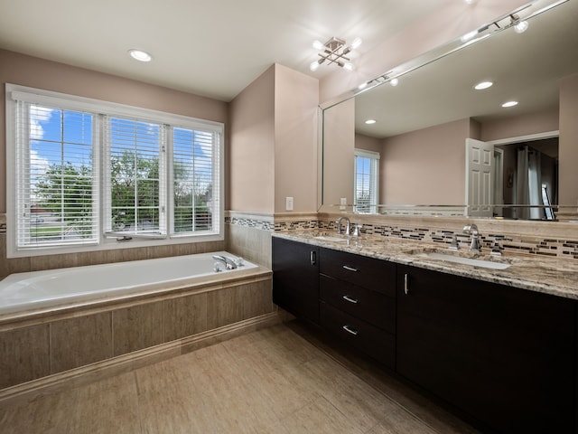 full bath featuring healthy amount of natural light, a garden tub, wood finished floors, double vanity, and recessed lighting