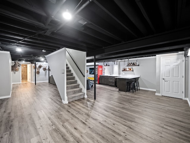 finished basement with bar with sink, stairway, baseboards, and wood finished floors