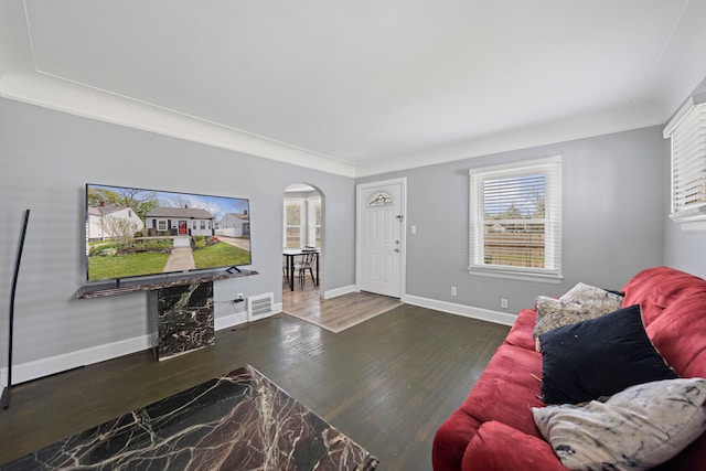 living room with arched walkways, wood finished floors, healthy amount of natural light, baseboards, and ornamental molding