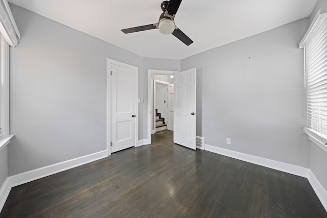 unfurnished bedroom with baseboards, multiple windows, dark wood-style floors, and a ceiling fan