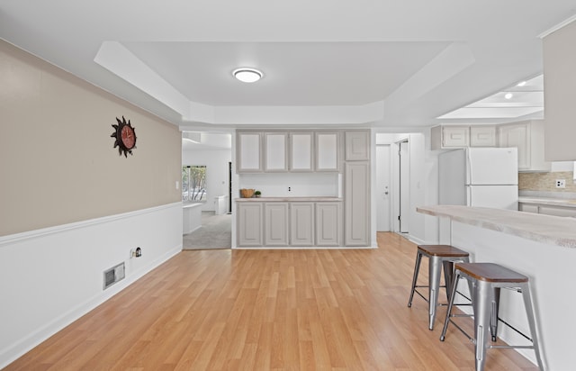 13488 Kingsville Dr, Sterling Heights, MI 48312 - kitchen with a tray ceiling, freestanding refrigerator, a breakfast bar, and light wood finished floors