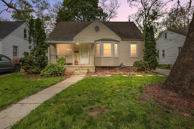 bungalow-style home featuring covered porch, a yard, and roof with shingles