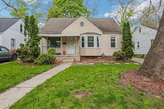 bungalow featuring covered porch, a front lawn, and a shingled roof