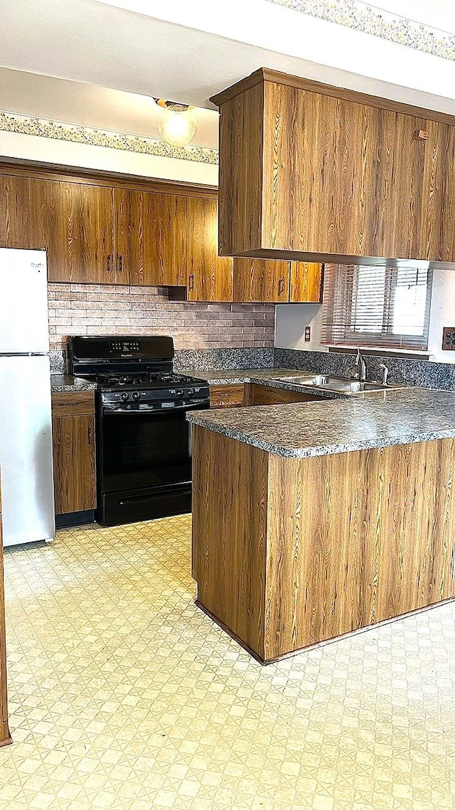 kitchen with freestanding refrigerator, black gas range oven, light flooring, decorative backsplash, and dark stone countertops