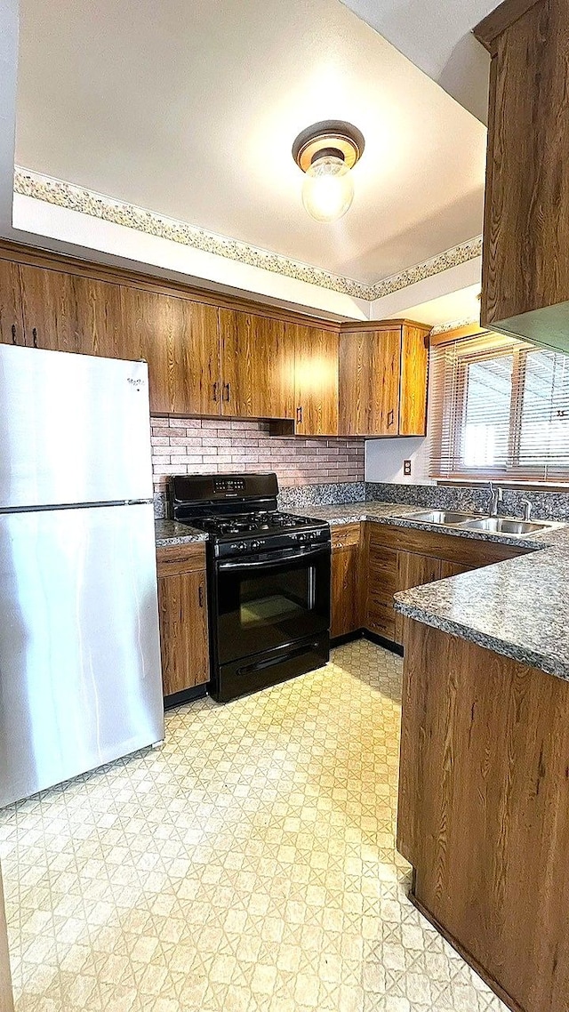 kitchen featuring freestanding refrigerator, black gas range, light floors, and a sink