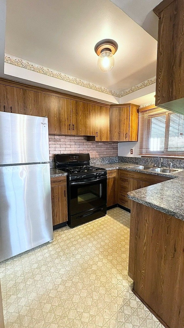 kitchen with freestanding refrigerator, gas stove, dark countertops, light flooring, and a sink
