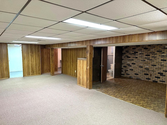 finished below grade area featuring wooden walls, a paneled ceiling, and light floors