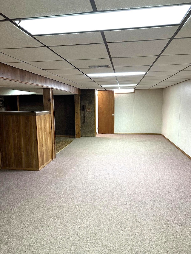finished basement featuring carpet, bar, wooden walls, and a drop ceiling