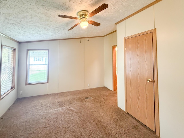 carpeted spare room with ornamental molding, a ceiling fan, plenty of natural light, a textured ceiling, and a decorative wall