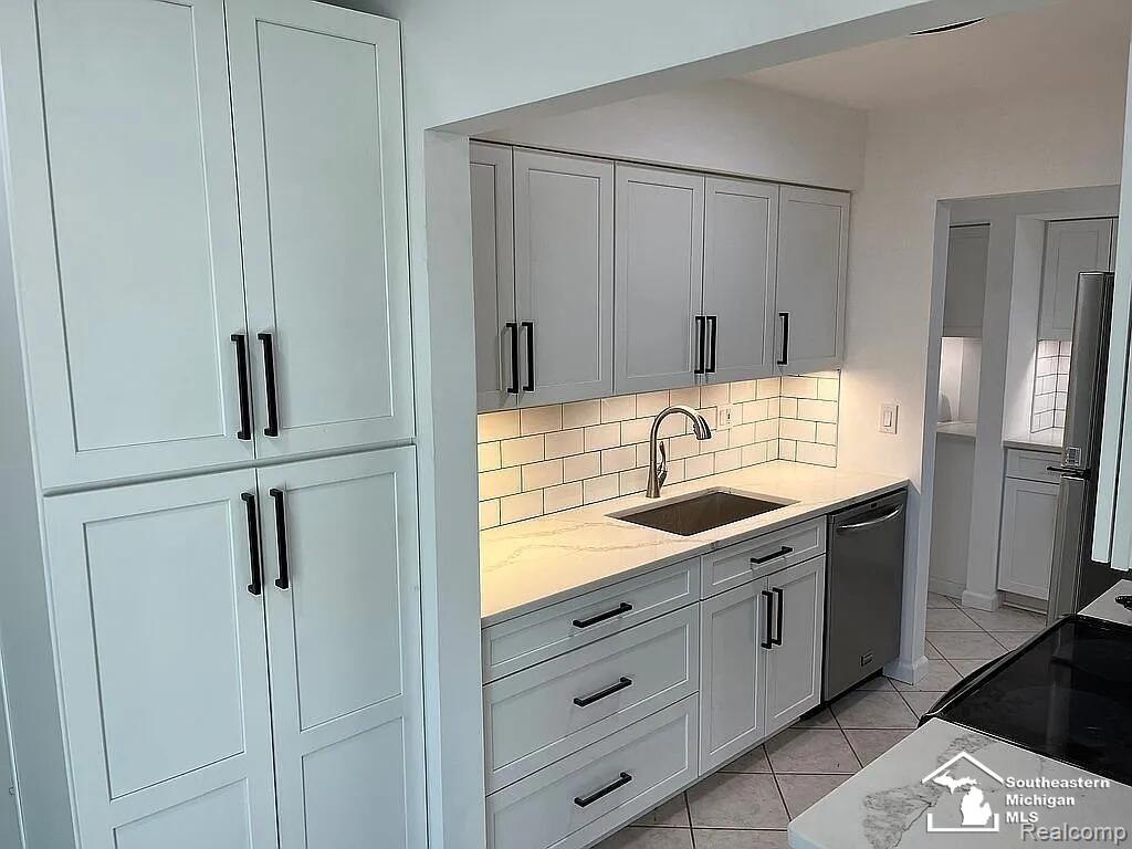 kitchen featuring a sink, dishwashing machine, backsplash, light stone countertops, and white cabinetry
