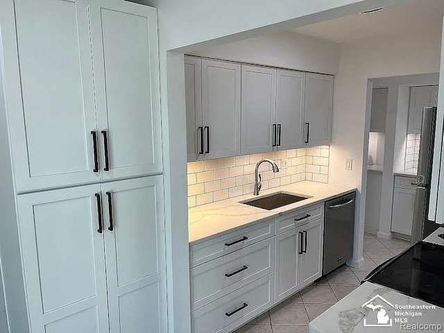 kitchen featuring a sink, dishwashing machine, backsplash, light stone countertops, and white cabinetry