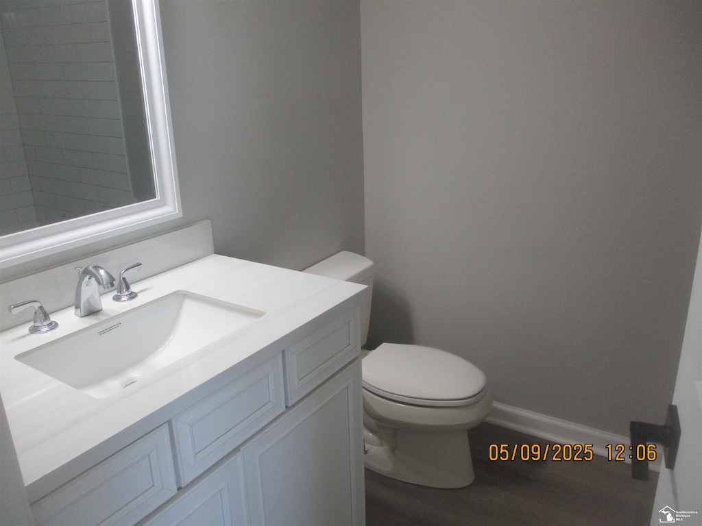 bathroom with toilet, vanity, wood finished floors, and baseboards