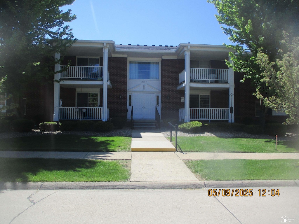 view of front of home with a balcony, brick siding, and a front lawn