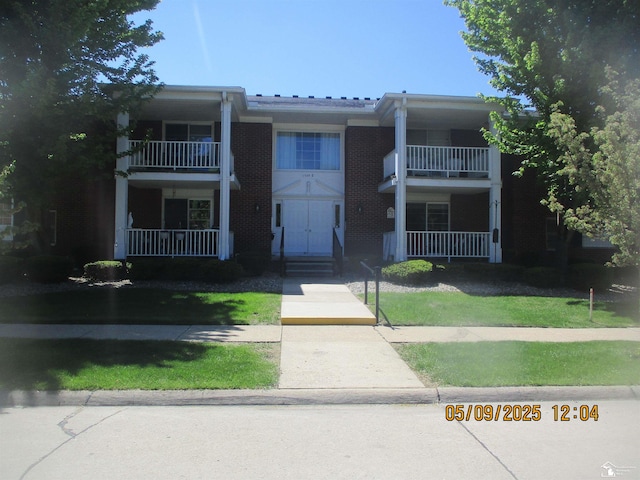 view of front of home with a balcony, brick siding, and a front lawn
