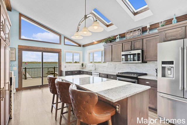 kitchen featuring stainless steel appliances, a skylight, high vaulted ceiling, a sink, and backsplash
