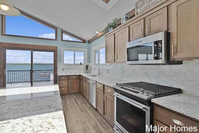 kitchen featuring stainless steel appliances, light wood-type flooring, backsplash, a sink, and light stone counters
