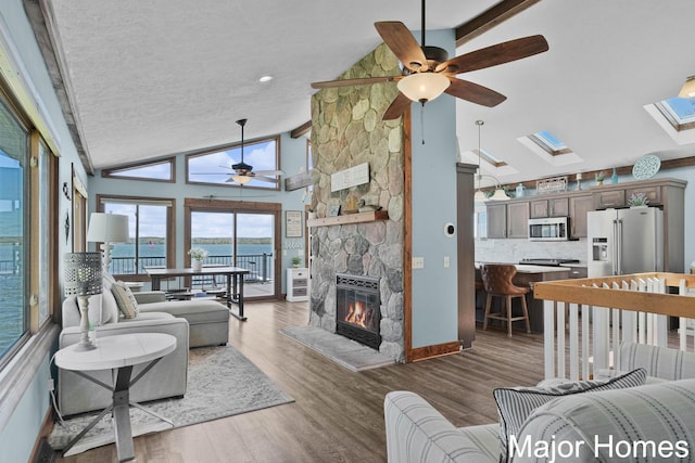 living area featuring a ceiling fan, a skylight, wood finished floors, a fireplace, and a water view