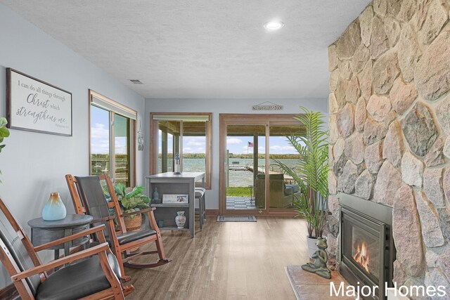 living area featuring a textured ceiling, wood finished floors, healthy amount of natural light, a water view, and a fireplace