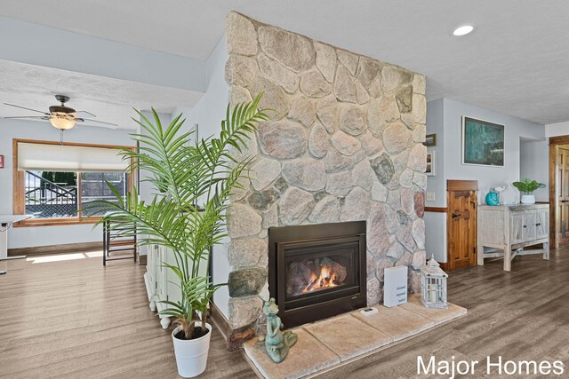living area featuring wood finished floors, a stone fireplace, ceiling fan, baseboards, and recessed lighting
