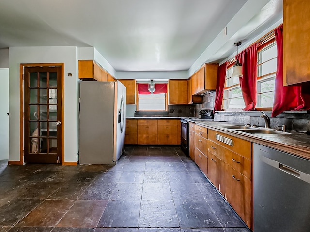 kitchen featuring appliances with stainless steel finishes, a sink, stone tile floors, decorative backsplash, and brown cabinets