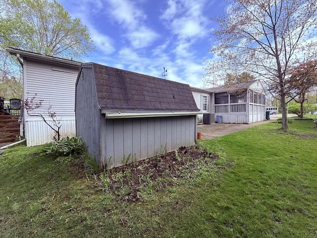 rear view of house with a sunroom, a yard, an outdoor structure, and roof with shingles