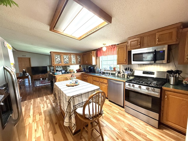 kitchen featuring appliances with stainless steel finishes, a textured ceiling, light wood finished floors, a sink, and brown cabinets