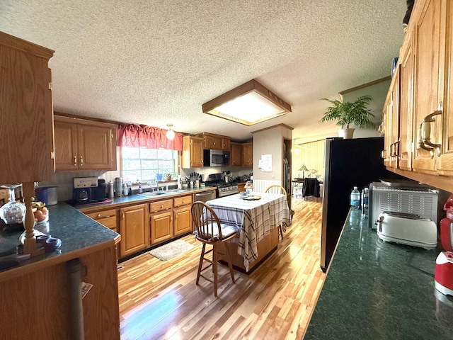 kitchen featuring stainless steel appliances, a textured ceiling, dark countertops, light wood-type flooring, and brown cabinetry