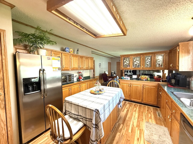 kitchen with stainless steel appliances, a textured ceiling, light wood-type flooring, brown cabinetry, and a sink