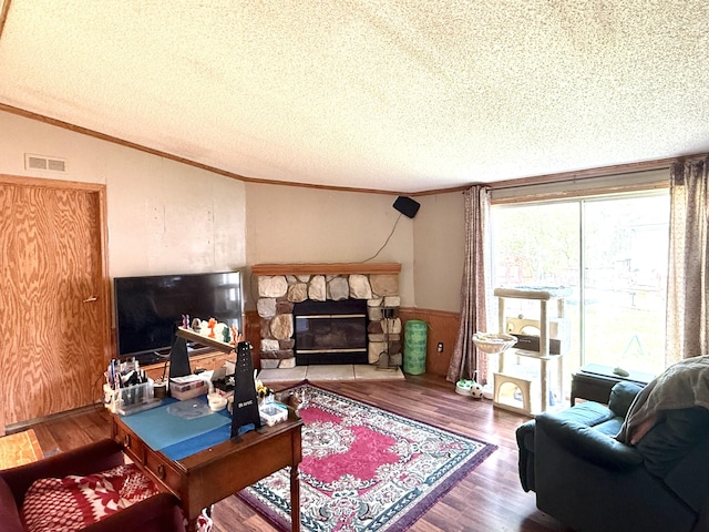 living room with ornamental molding, wood finished floors, a textured ceiling, a wainscoted wall, and a stone fireplace